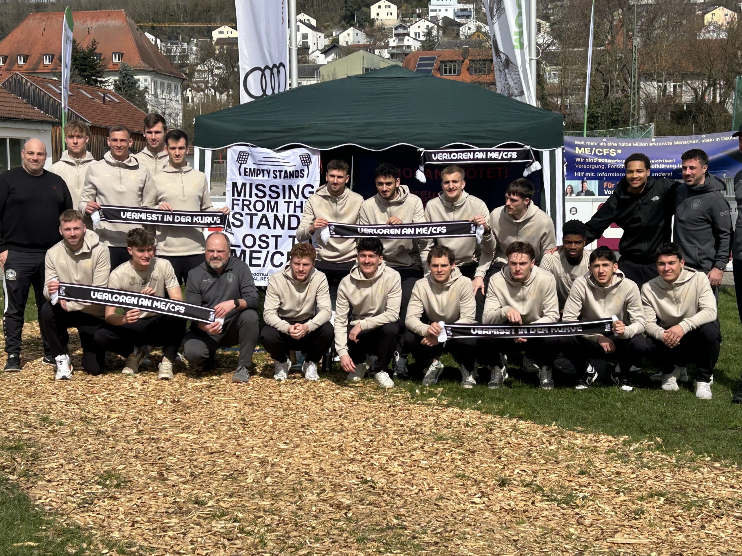 Generiert: Eine Gruppe von Männern steht vor einem grünen Zelt und hält Banner hoch. Die Banner tragen die Aufschriften "VERMISST IN DER KURVE" und "VERLOREN AN ME/CFS". Die Gruppe repräsentiert Fußballfans mit ME/CFS, Long COVID & Post-Vac.